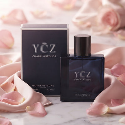 A 50ml YCZ perfume bottle resting on a white marble surface surrounded by blush pink silk and rose petals.